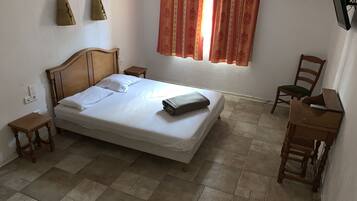 A bedroom with a wooden bed, a small bedside table, a chair, a desk, and a window with curtains.