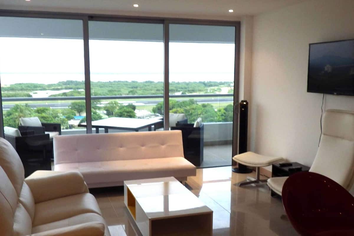 A modern living room with a sofa, a red chair, a coffee table, and a TV mounted on the wall.
