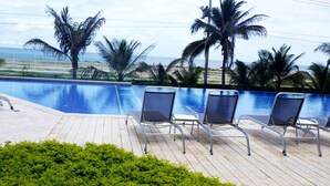 Zona junto a la piscina con sillones de descanso y vista a la playa y al océano.