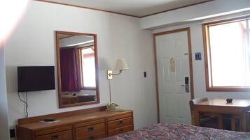 A hotel room with a bed, a desk, a dresser, a TV mounted on the wall, and a window with curtains.