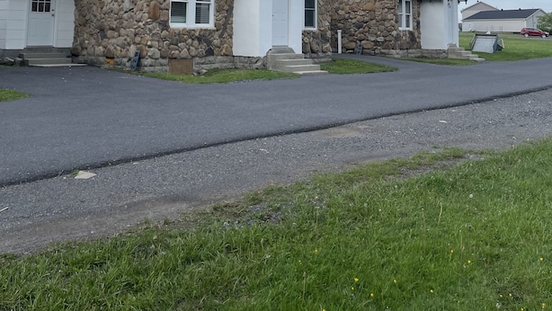 Une rangée de maisons en pierre à deux étages, avec des toits bruns et des éléments décoratifs blancs, chacune dotée d'un porche à l'avant et d'un petit jardin.