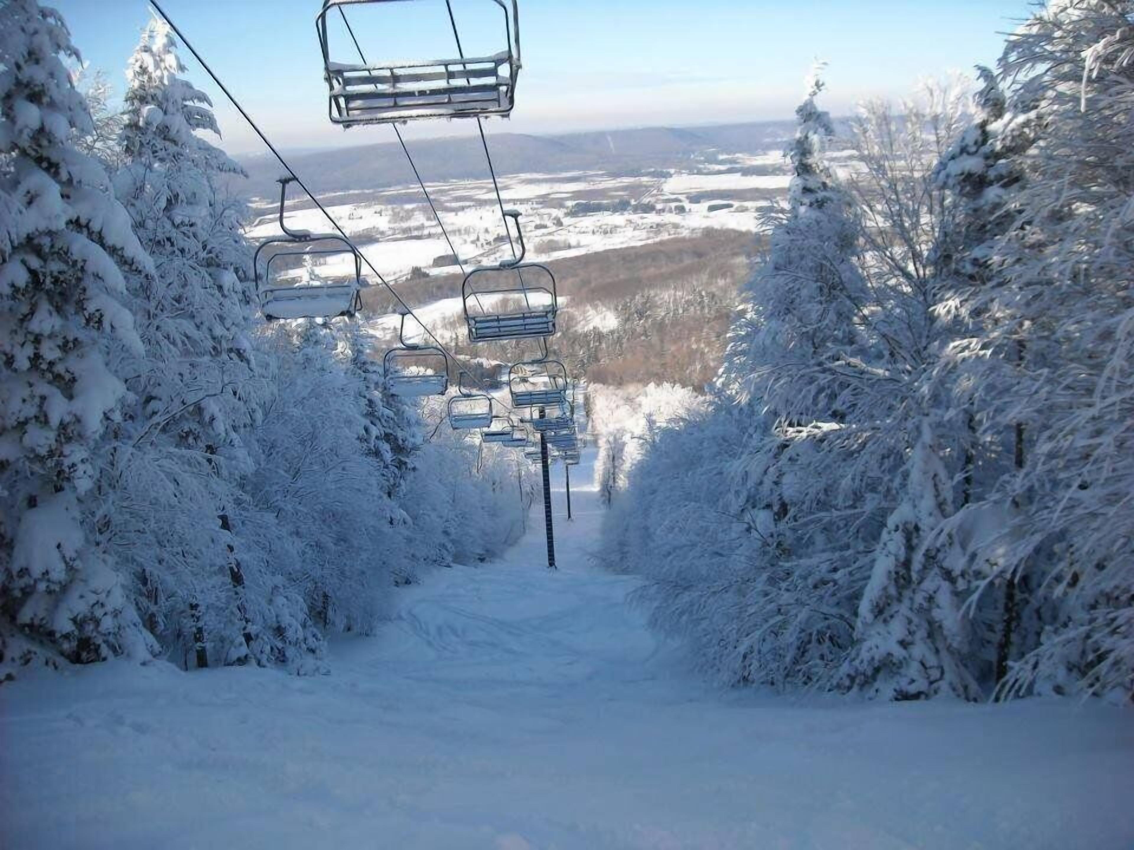 A snow-covered ski lift with chairs suspended from cables, surrounded by trees and a snowy landscape.