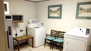 Une petite buanderie équipée d’un lave-linge, d’un sèche-linge, d’un four à micro-ondes et de deux chaises.