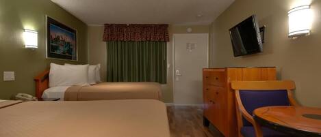Ett hotellrum med två sängar, ett skrivbord med en stol, en byrå, en tv som är monterad på väggen och en tavla på väggen.