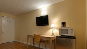 A compact room with a desk, a chair, a television mounted on the wall, a microwave, and a refrigerator. - Vagabond Inn Bakersfield North (Bakersfield)