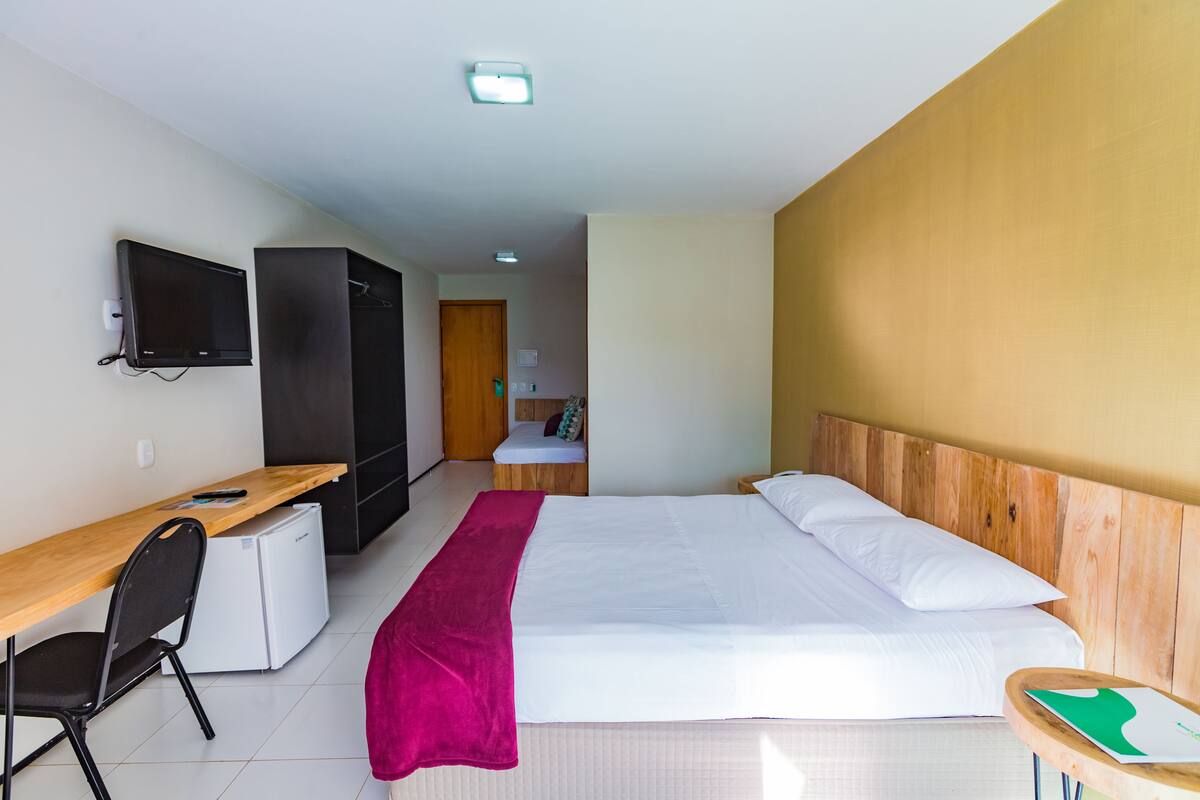 A hotel room with a bed, a desk, a chair, a TV, and a wardrobe.