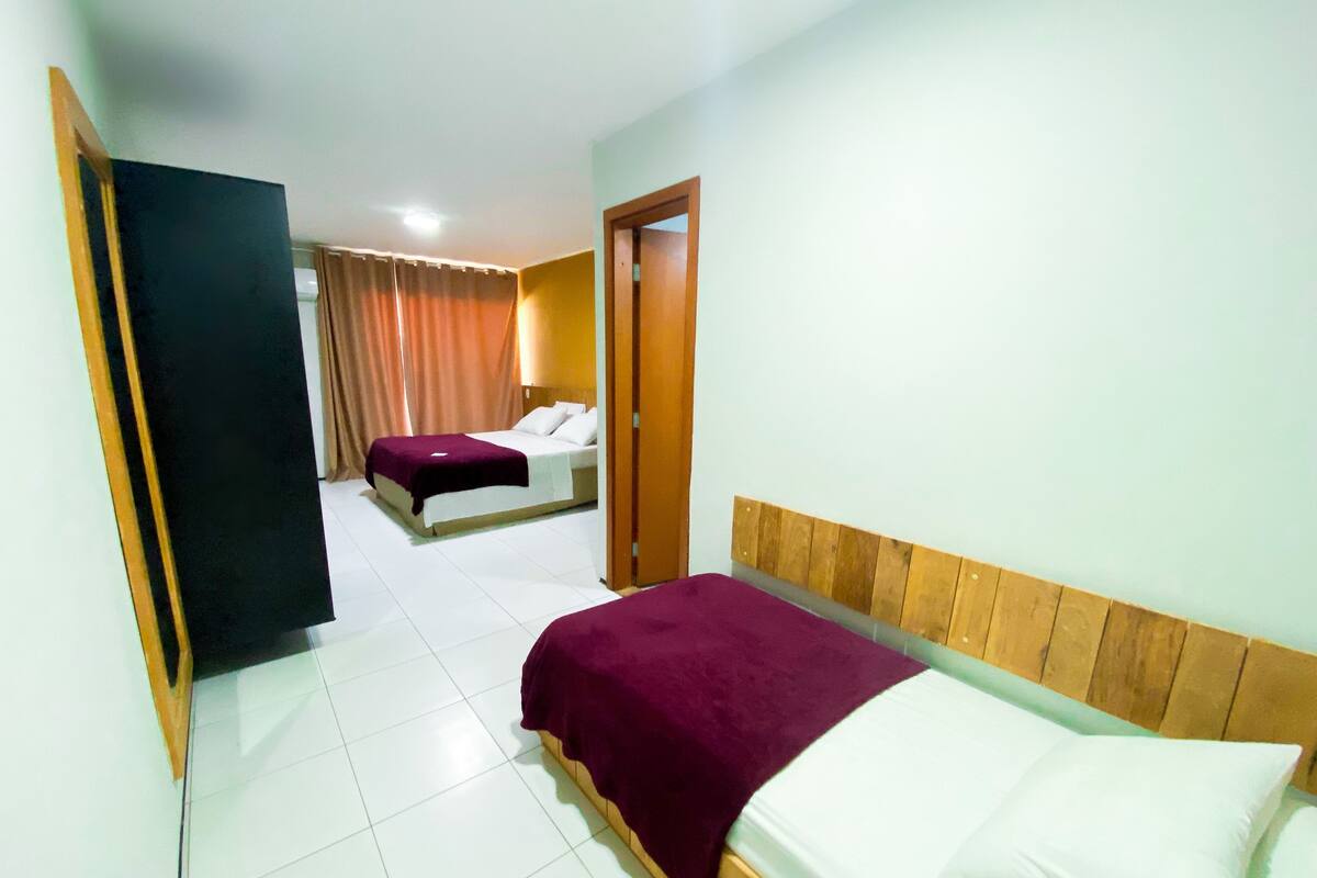 A hotel room with two beds, a wooden headboard, a tiled floor, and a door leading to another room.