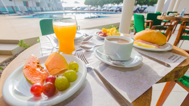Desayuno con vistas a la piscina, incluye un plato con melón, uvas, un sándwich y un vaso de zumo de naranja.