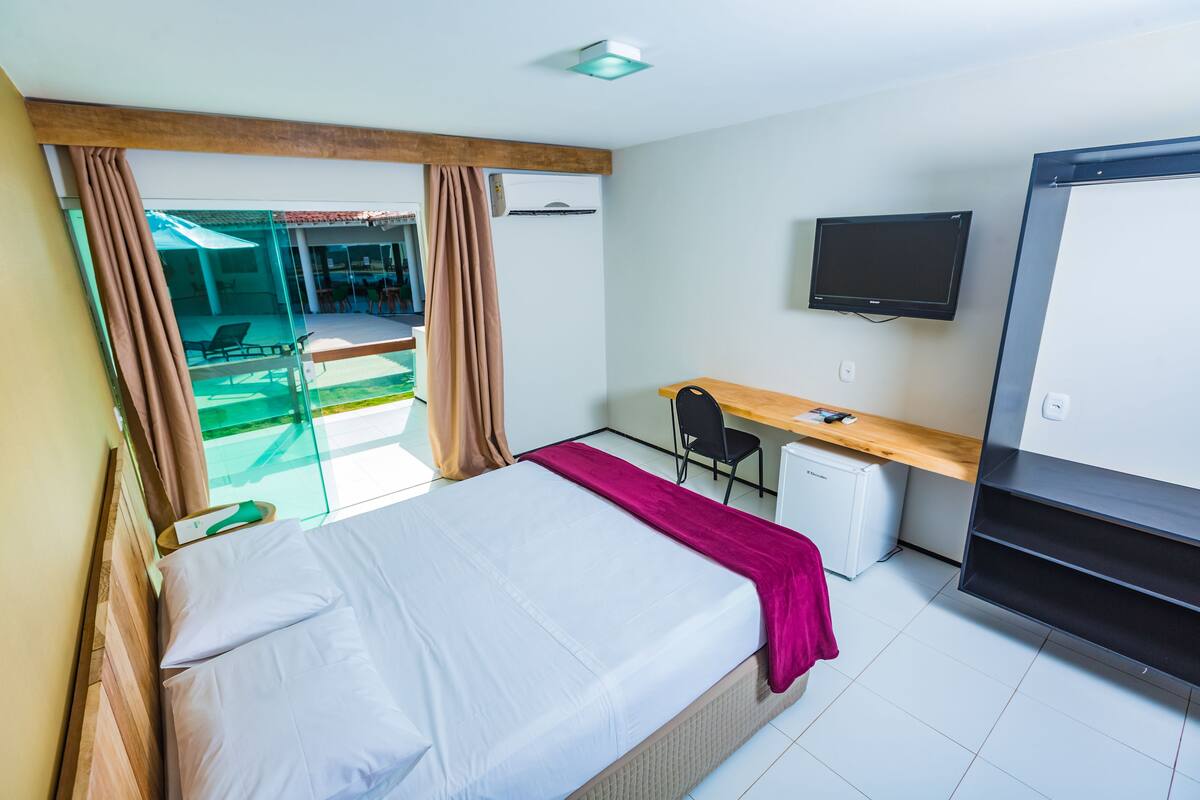 A hotel room with a bed, a desk, a television, and a view of an outdoor area.