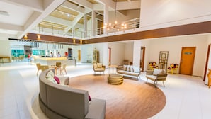 Un lobby espacioso con una zona de estar central, una recepción y un techo alto con luz natural.