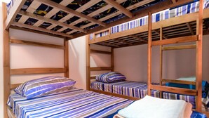 A bunk bed room with striped bedding and a wooden ceiling.