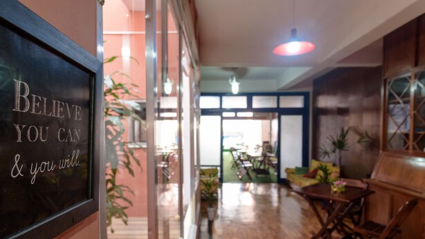 A spacious indoor area with a wooden floor, a glass partition with motivational writing, and a view of a dining area with tables and chairs.