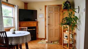 Una sala de estar acogedora con chimenea, televisor, mesa de comedor con sillas y una puerta que da a otra habitación.