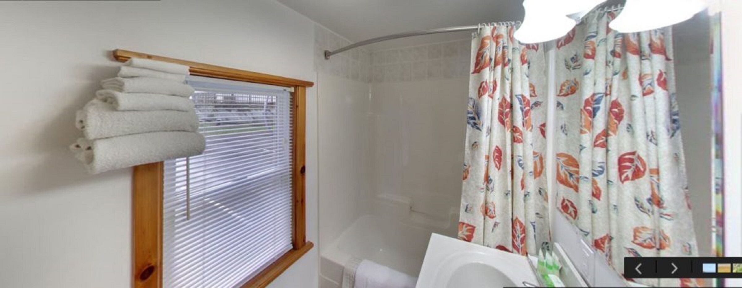Un baño con ducha, una ventana con persianas y una cortina con estampado de peces.