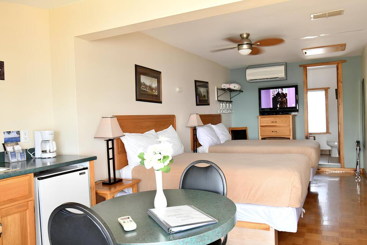 Una habitación de hotel con una cama, un escritorio con cafetera, un televisor y un ventilador de techo.