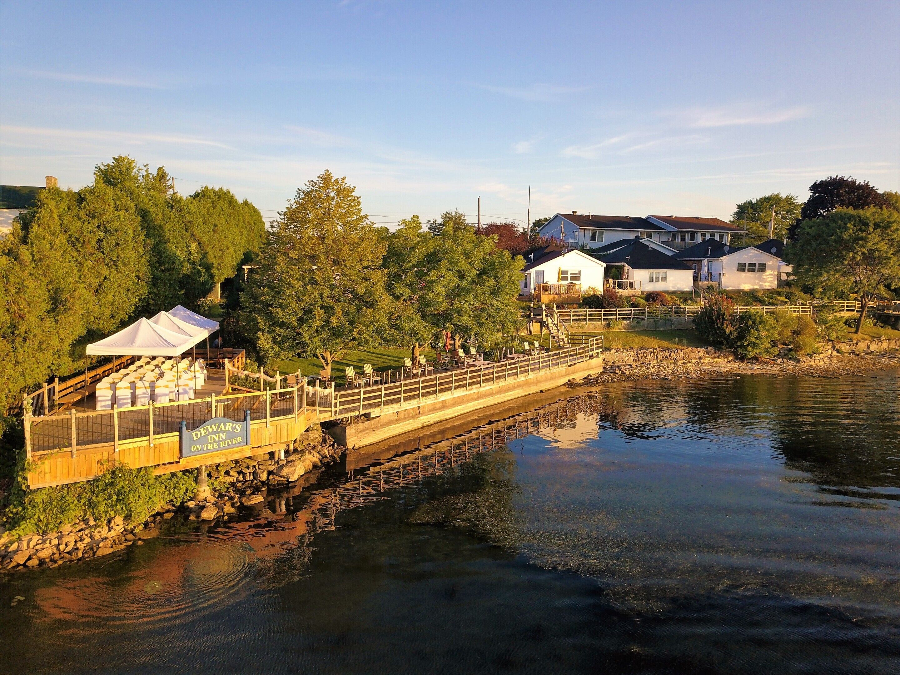 Una passeggiata lungo il fiume con un ponte di legno, una tenda bianca e un cartello per Dewar's Inn.