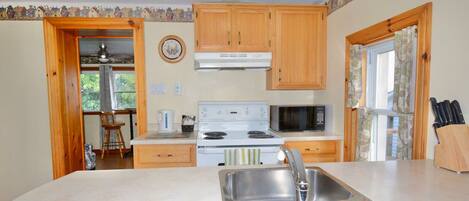 A kitchen with wooden cabinets, a white stove, a sink, and a microwave.