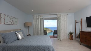 A bedroom with a large bed, a TV mounted on the wall, and a view of the ocean through an open door. - Xhale Luxury Villa (Gros Islet)