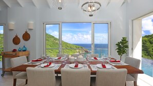 A dining area with a view of the ocean and hills, a wooden table set for four, and a plant on the right. - Xhale Luxury Villa (Gros Islet)