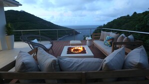 A deck with a fire pit, outdoor seating, and a view of the ocean. - Xhale Luxury Villa (Gros Islet)