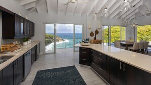 A modern kitchen with a large island, dark cabinets, and a view of the ocean. - Xhale Luxury Villa (Gros Islet)