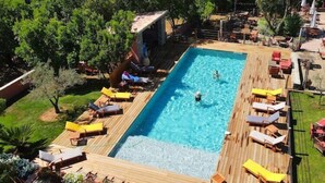 Ein rechteckiger Pool mit Holzterrasse, umgeben von Liegestühlen und Sonnenschirmen, eingebettet in eine üppige, grüne Landschaft.