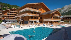 Ein Chalet-Hotel aus Holz mit Schwimmbad, mehreren Balkonen und Sitzgelegenheiten im Freien.