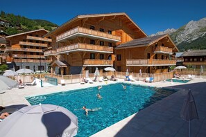 A wooden chalet-style hotel with a swimming pool, multiple balconies, and outdoor seating areas. - Modern Alpine Apartment (La Clusaz)