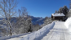 Eine verschneite Bergstraße, die zu einer Hütte mit blauem Himmel führt.