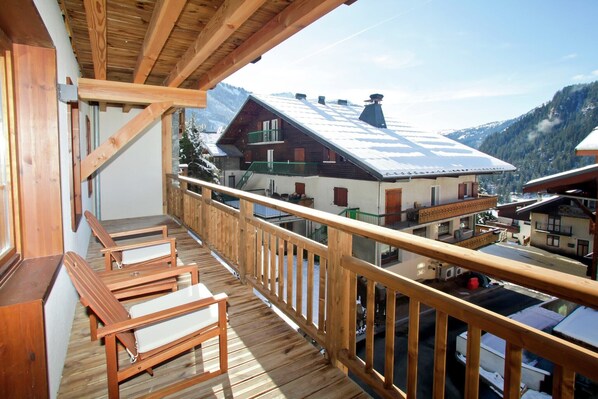 A wooden balcony with a view of a mountain landscape and buildings.