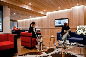 A modern lounge area with seating, a television screen, and a glass table with a teapot and cups.