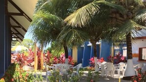 Un patio con césped, palmeras y zona de estar al aire libre con sillas de plástico blancas.