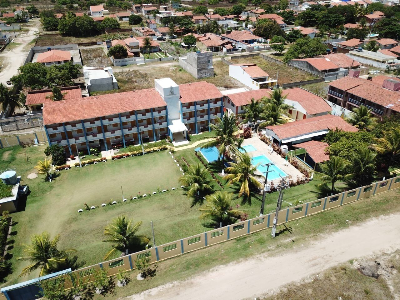 Vista aérea de una zona residencial con un edificio grande que tiene piscina, rodeado de vegetación y palmeras.