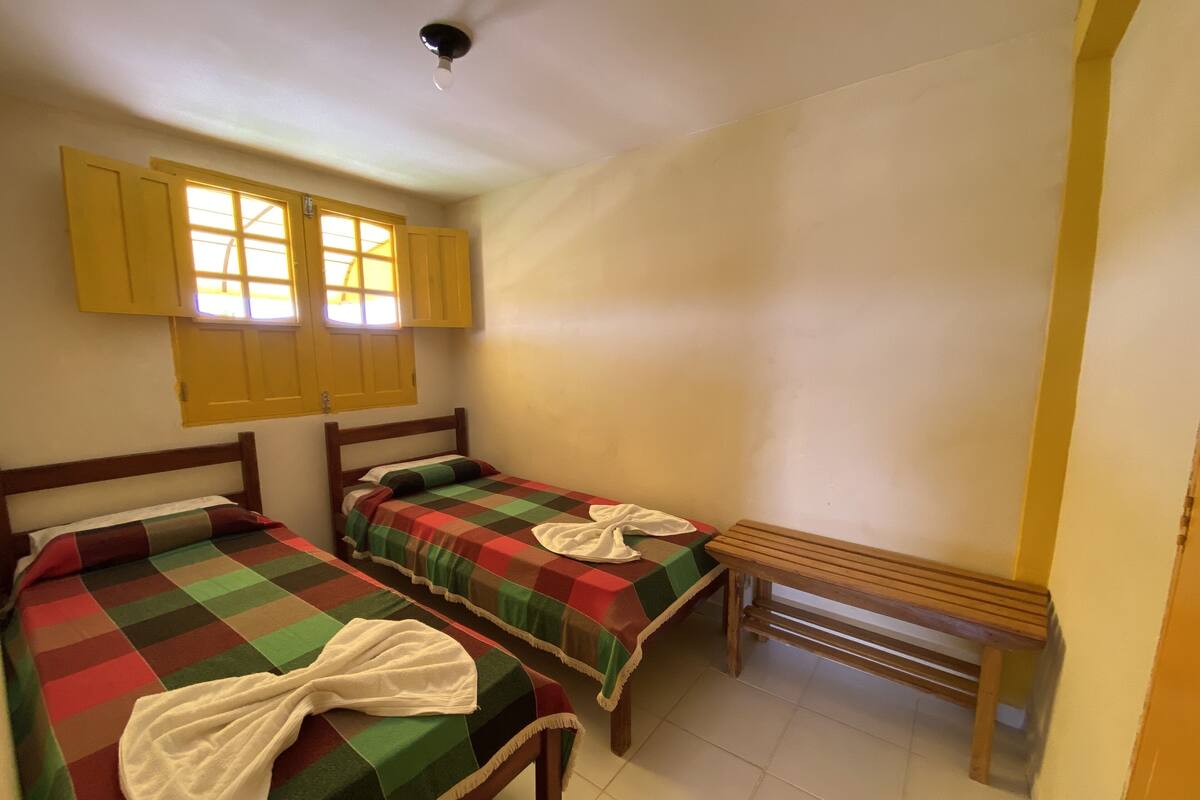 A room with two single beds, a bench, and a window with yellow shutters.