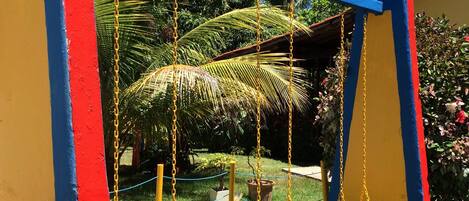 A swing set with yellow seats and blue and red supports, surrounded by greenery and a clear sky.