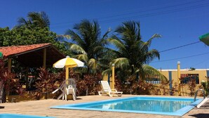 Un área de piscina con dos piscinas, sillas de descanso y una zona de estar cubierta con sombrilla.