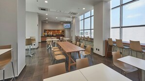 A spacious dining area with multiple tables and chairs, a kitchen in the background, and large windows providing natural light. - City Express by Marriott Ciudad De México La Raza (Mexico City)