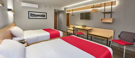 Habitación de hotel con dos camas, un escritorio, una silla, un espejo y un equipo de aire acondicionado.