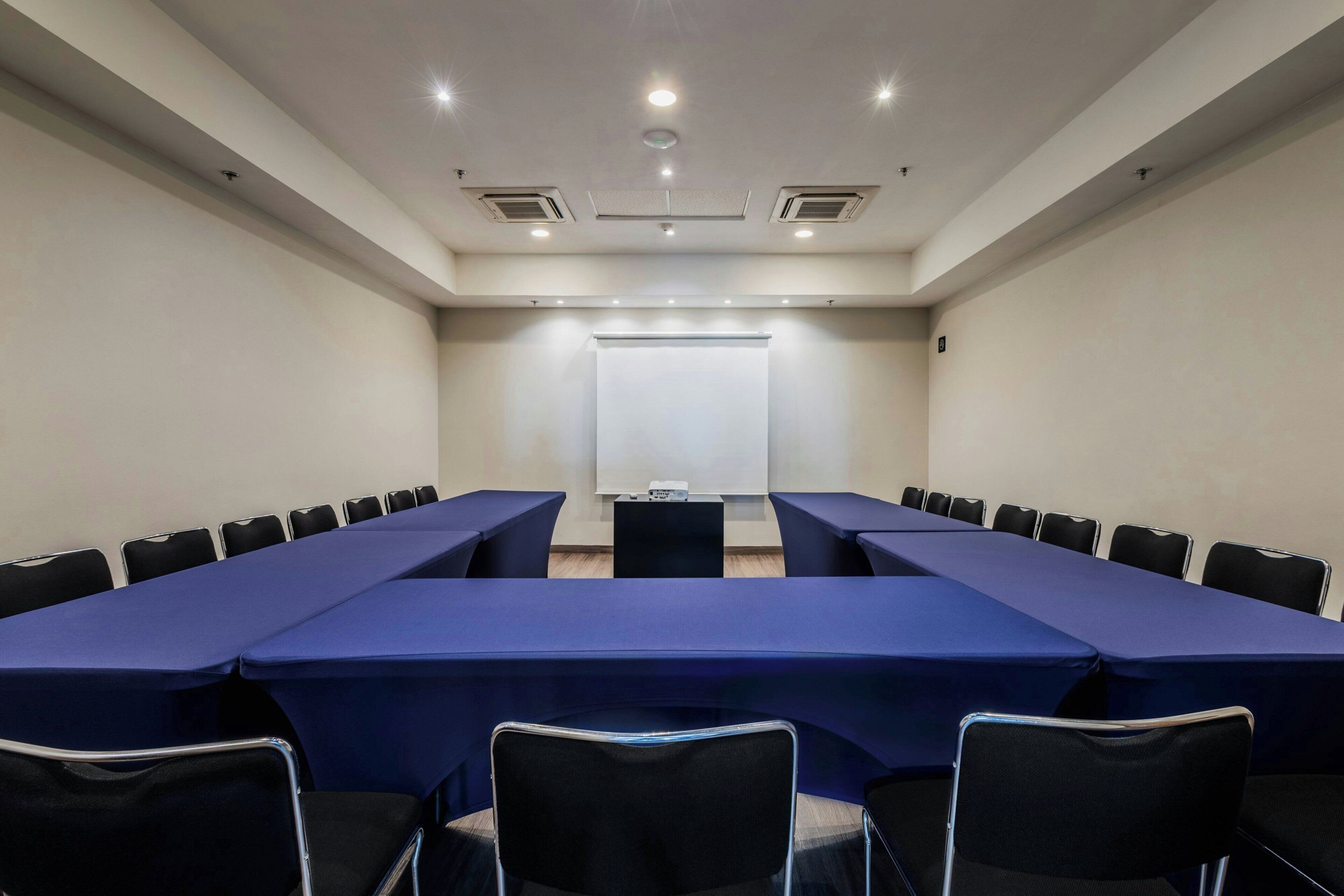 Une salle de conférence équipée d’une longue table, de chaises, d’un écran de projection et d’un tableau blanc.