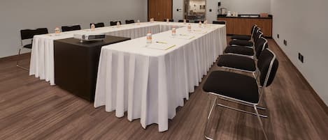 Un salón de conferencias con una larga mesa, sillas y una kitchenette al fondo.