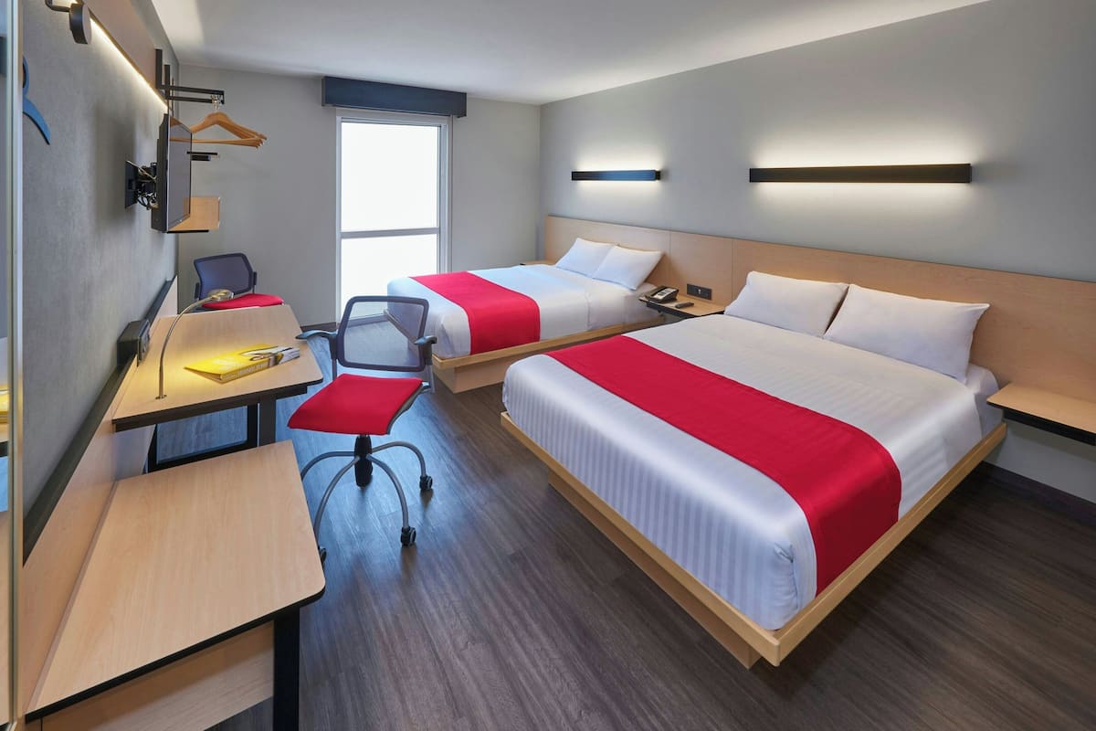Hotellihuone, jossa on kaksi sänkyä, työpöytä, tuoli, työpöytälamppu ja ikkuna.