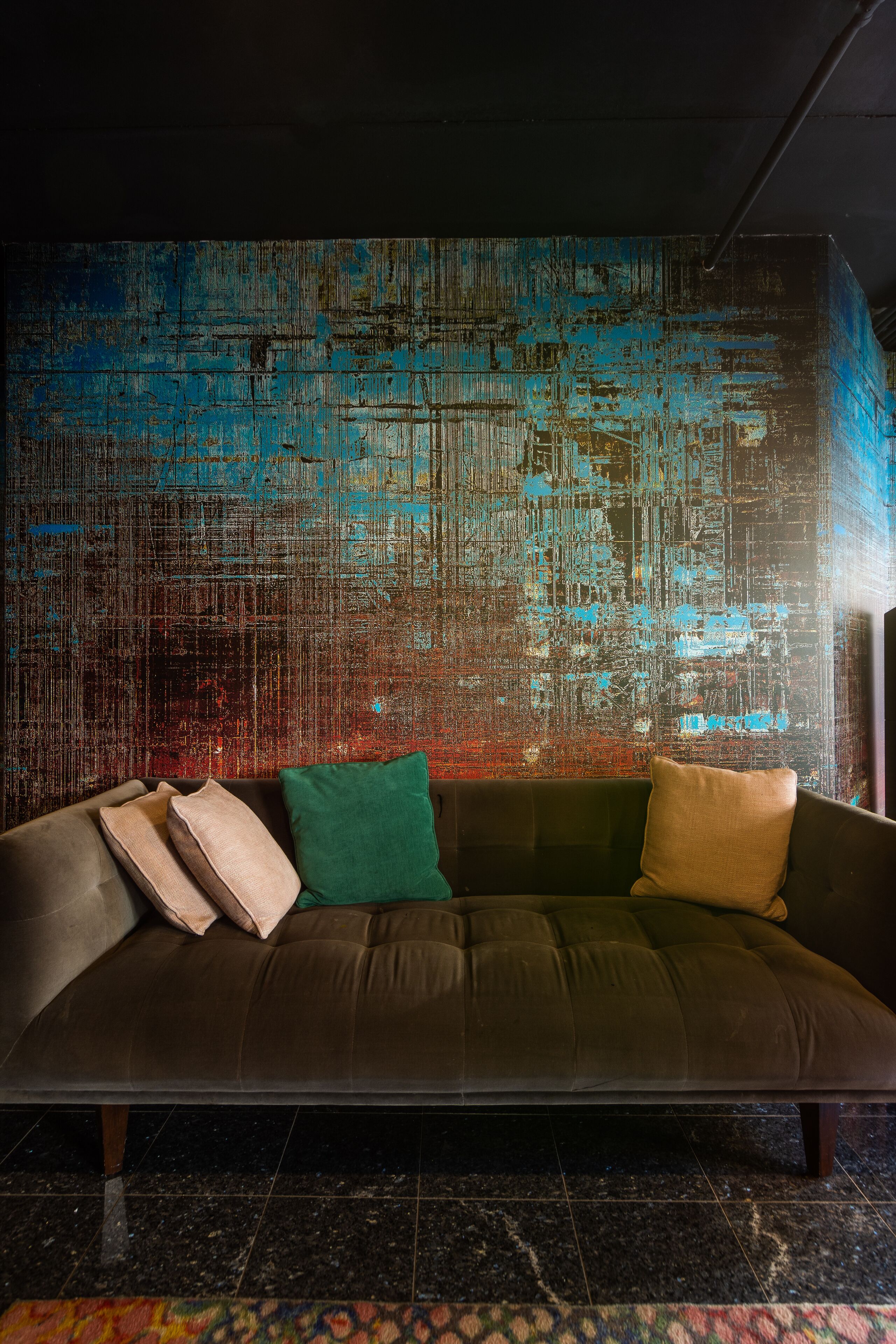 Un salon moderne avec un canapé marron foncé, des coussins verts et beige, et un mur bleu à texture.