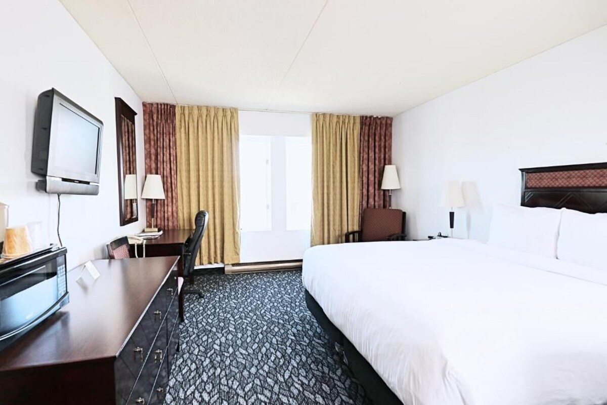 A hotel room with a bed, a desk with a television, a chair, and a lamp.