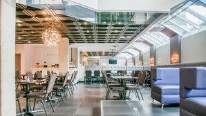 Un ristorante moderno con soffitti alti, pareti in vetro e diverse opzioni di posti a sedere, tra cui tavoli e panche imbottite.