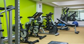 Una palestra con diverse attrezzature per esercizi, tra cui tapis roulant e cyclette, con una parete verde sullo sfondo.