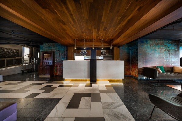 Una moderna hall con soffitto in legno, una reception, una poltrona e un pavimento decorato.