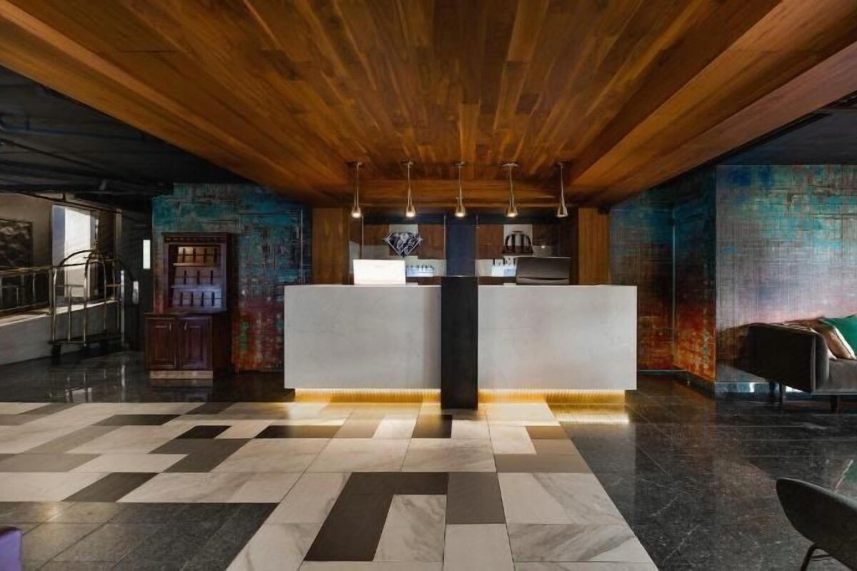 A modern lobby with a checkered floor, a reception desk, a bar area, and a seating area with a sofa and chairs.
