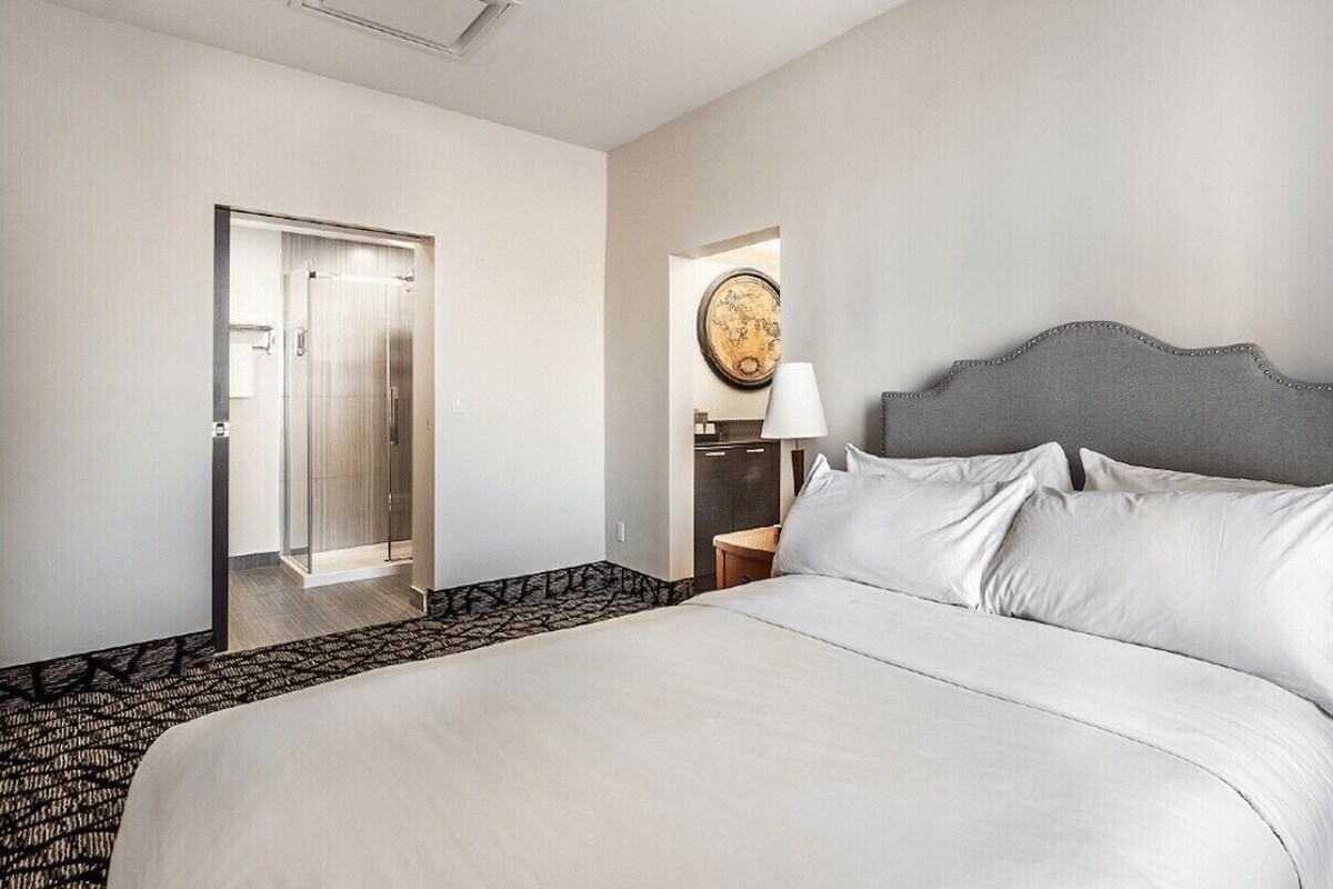 A hotel room with a bed, two bedside tables with lamps, a door, and a mirror.