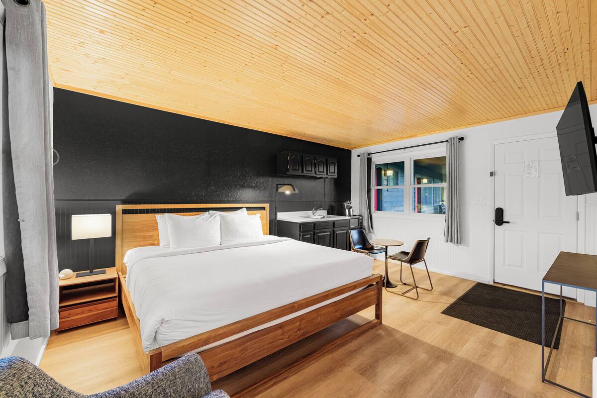 Een moderne slaapkamer met een houten plafond, een groot bed, een bureau en uitzicht op de omgeving.