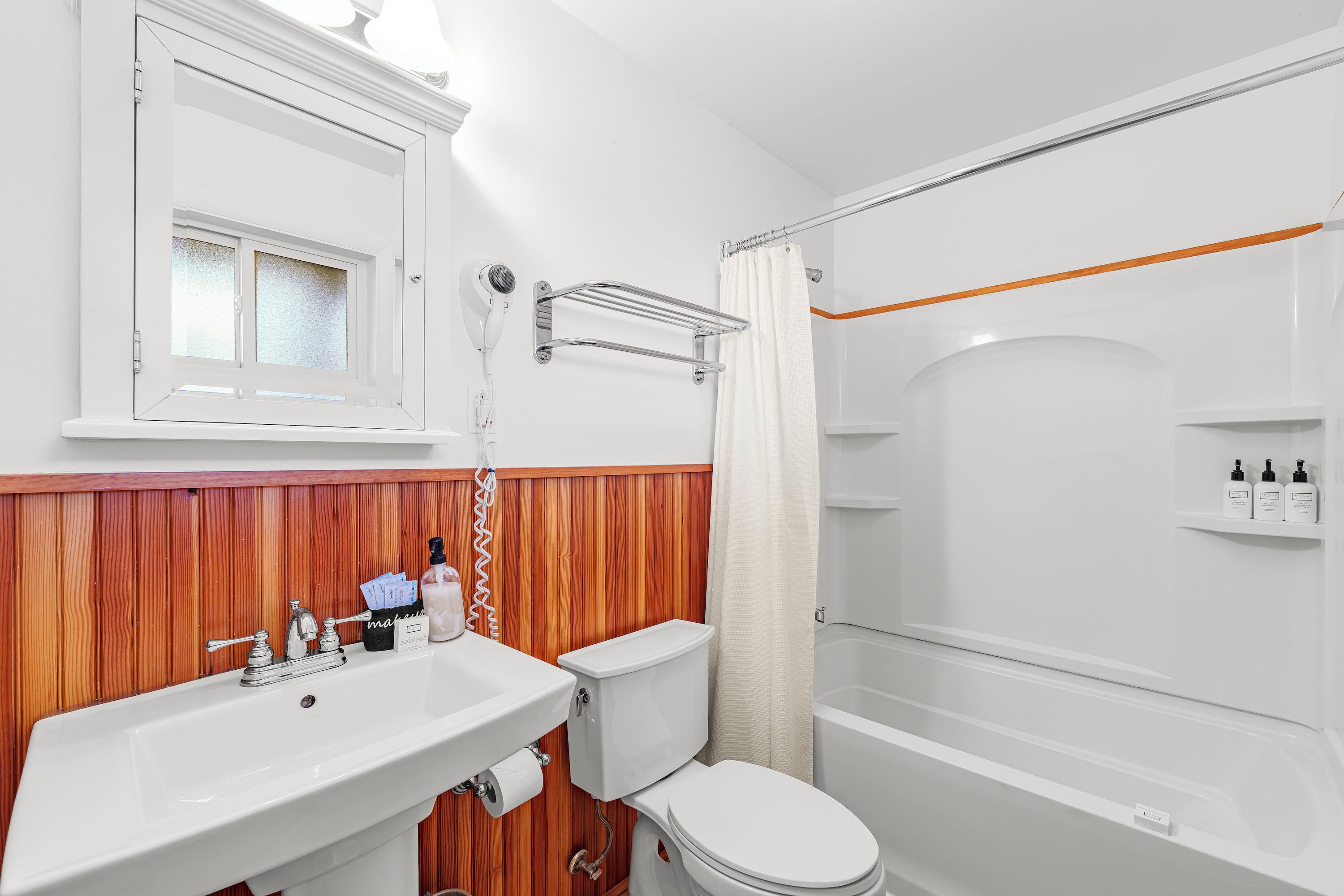 A bathroom with a wooden vanity, a white sink, a toilet, and a shower area.